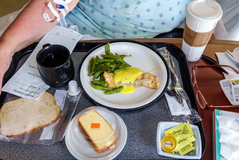 A photo of a tray of food in front of a hospitalized woman.