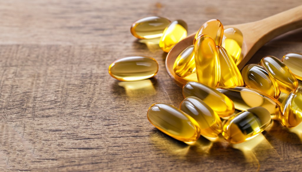 Fish oil and vitamin D supplement capsules on a wooden background.