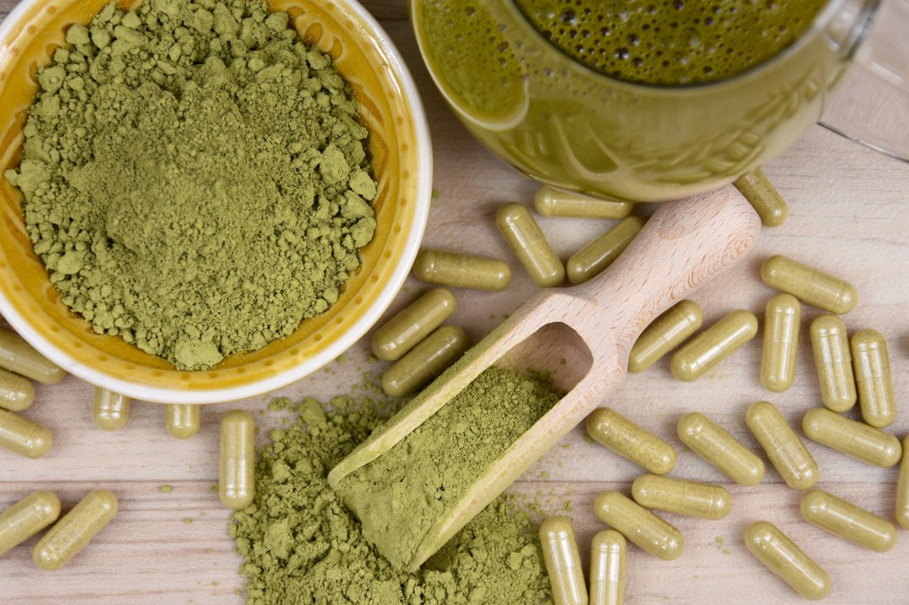 Kratom powder in a bowl and scoop, kratom capsules, and a glass of kratom drink.