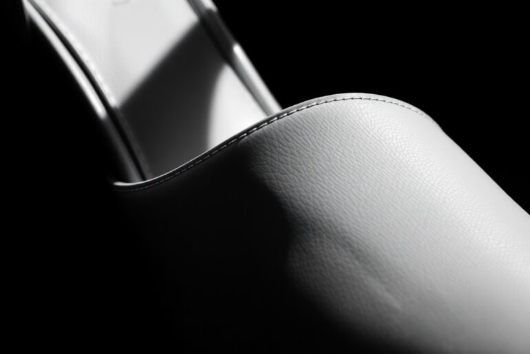 An extreme close-up photograph of the glossy, high-contrast texture of a white patent leather Prada slingback pump, capturing the shoe