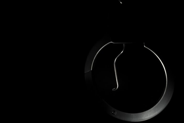 An extreme close-up photograph of a police badge or handcuffs lit by a harsh, direct camera flash against a pitch-black background, conceptually representing the investigative nature of modern policing and the need for officer wellness initiatives.