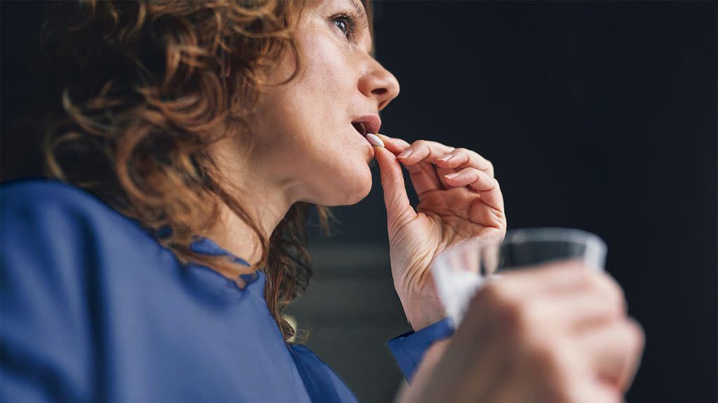 A woman gets ready to swallow a vitamin D supplement with a cup of water in her hand