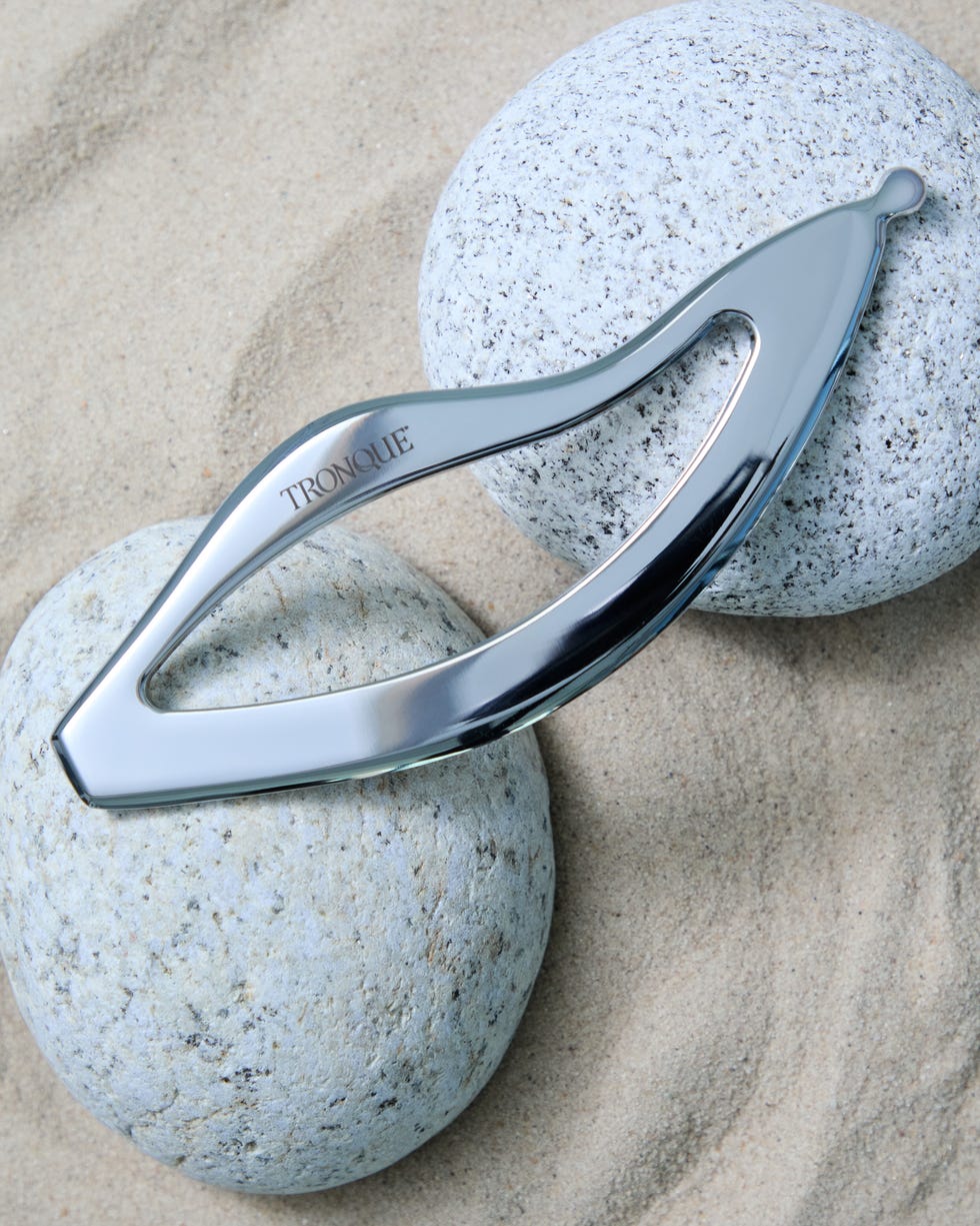 A sleek, metallic tool is placed on smooth, round stones on a sandy surface.