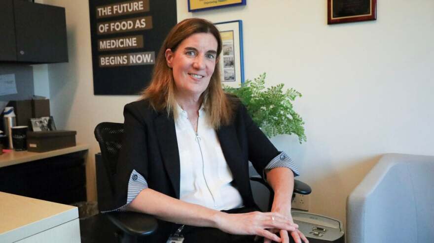 A woman in a black blazer poses for a picture at a desk.