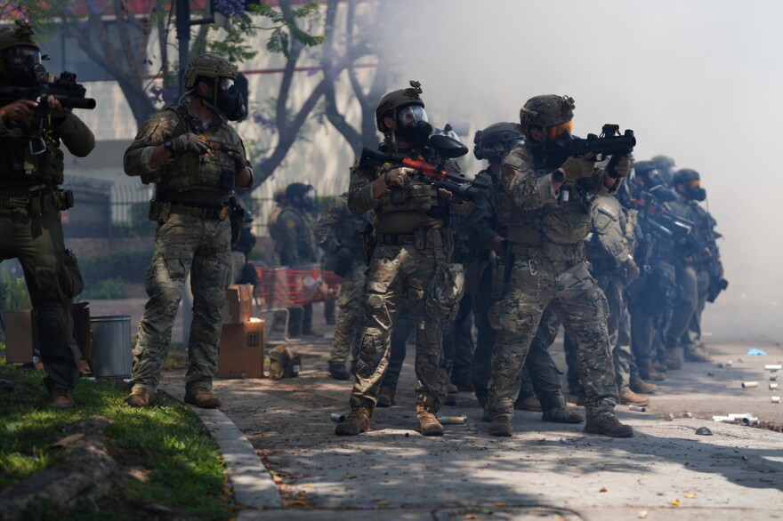 People wearing military outfits hold weapons towards a crowd.