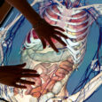 Two hands are touching a table that is a lit up screen of the human body