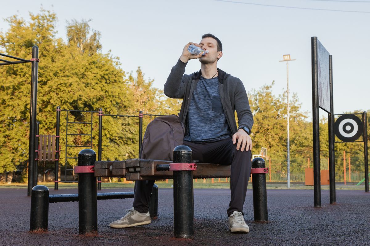 Athletic man drinking water. Morning workout outdoor. Thirsty athlete pouring water