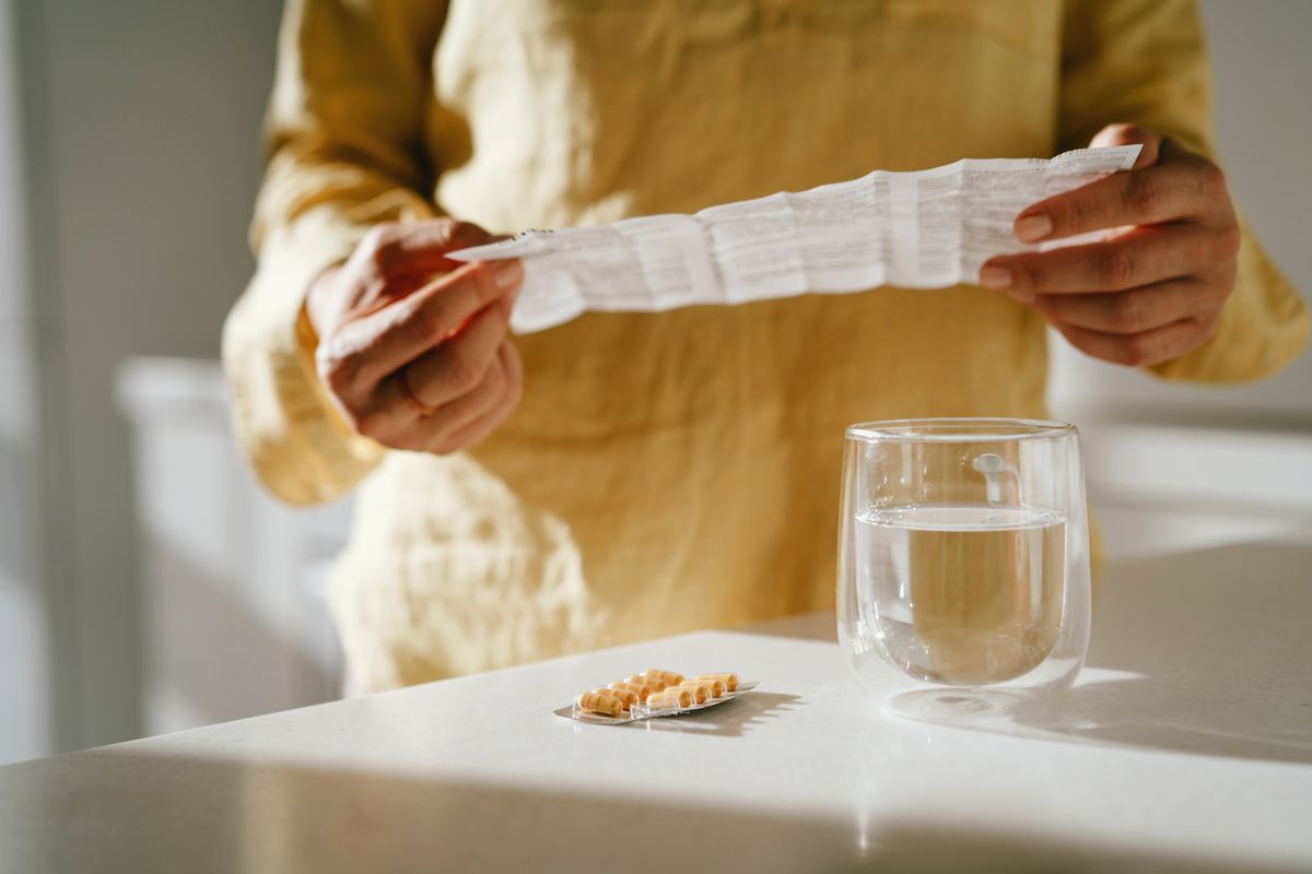 Mature woman standing at a table with green pills in her hand. Taking vitamins, macro elements and bioactive supplements to maintain health. Prevention of colds during an epidemic. The first symptoms of incipient menopause are hypotension or hypertension, hot flashes.
