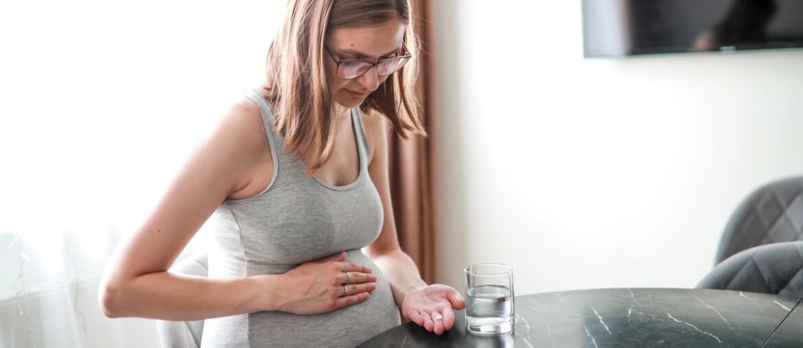 pregnant woman with a sore stomach drinks a tablet at a table at home.