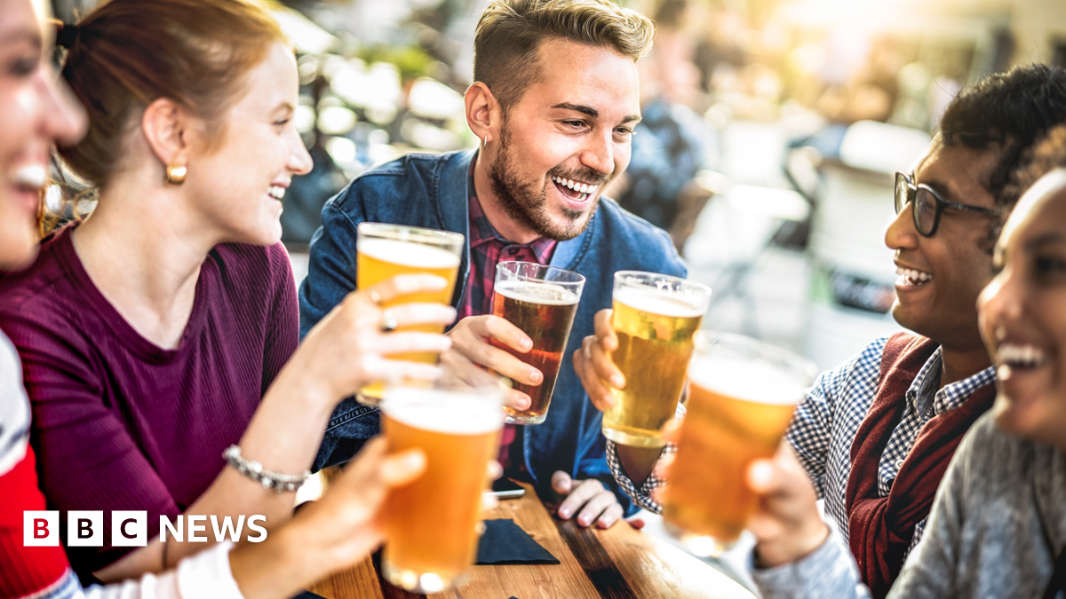 A group of happy men and women enjoying pints of beer whilst seated at a table outside a pub