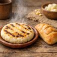 Steaming Colombian arepa and a piece of bread on a rustic wooden table, illustrating staple foods targeted by mandatory fortification in Colombia.