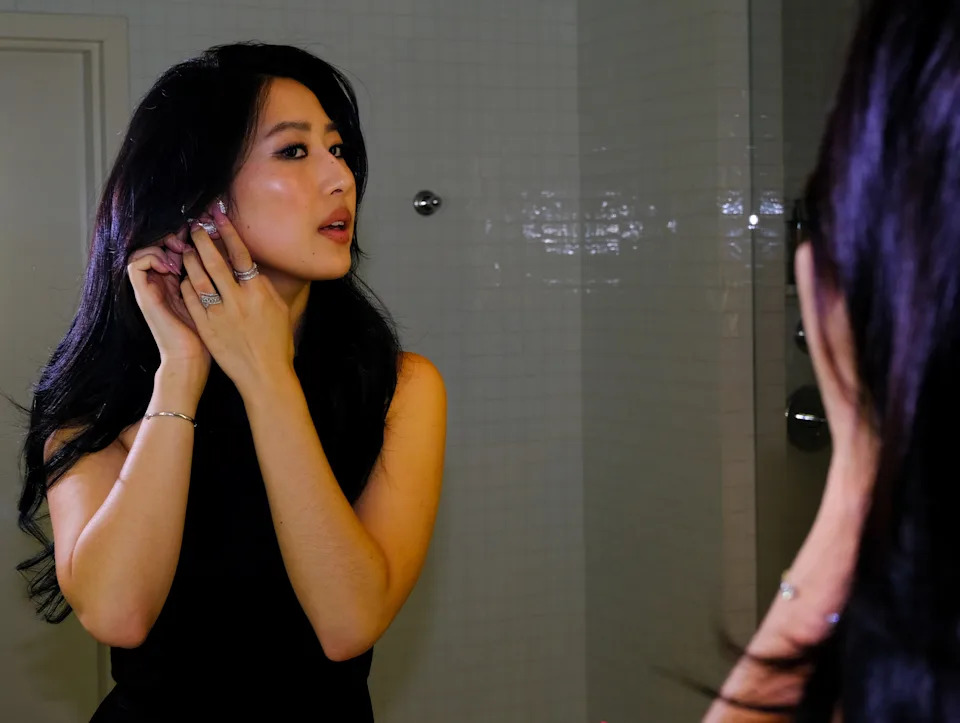 Actress Mabel Li is photographed getting ready for The Testaments L.A. premiere. She is looking into a mirror adjusting her earrings. 