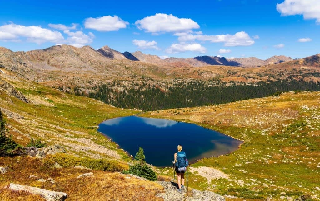 a woman stands on a rock looing at at treasure vault lake on the missouri lakes fancy lake loop