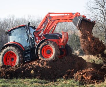 A promotional photo of a Kioti tractor perched atop a pile of dirt dumping dirt from its bucket.