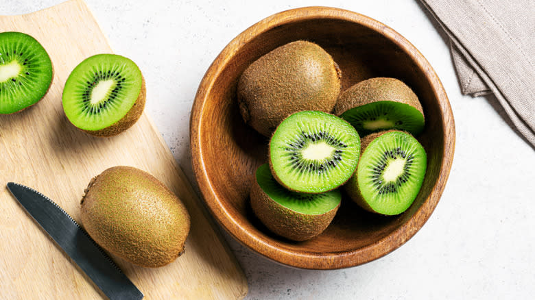 Kiwi fruit in a wooden bowl and on a cutting board, cut in half