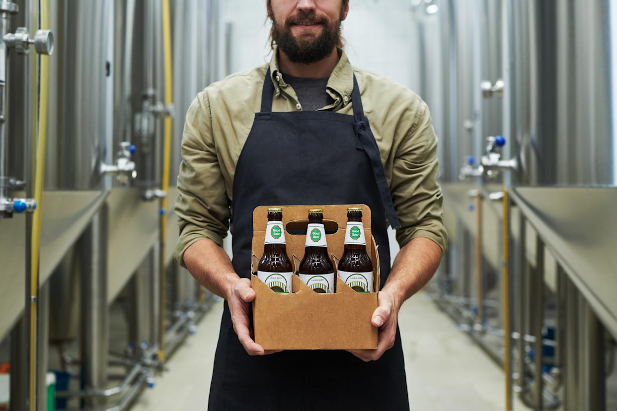A man in an apron holding a six-pack of 