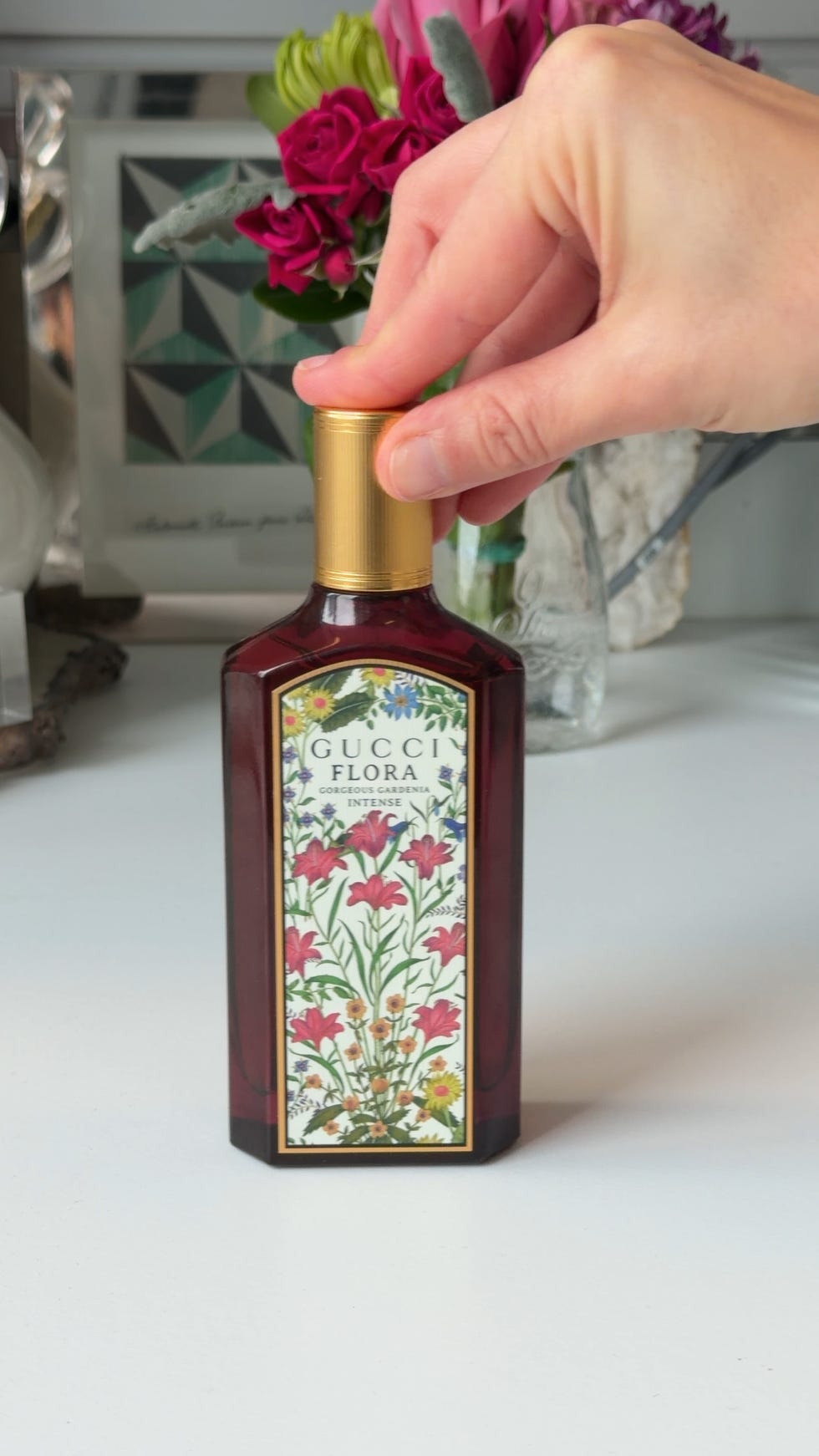 Bottle of Gucci Flora perfume being held, featuring floral design.