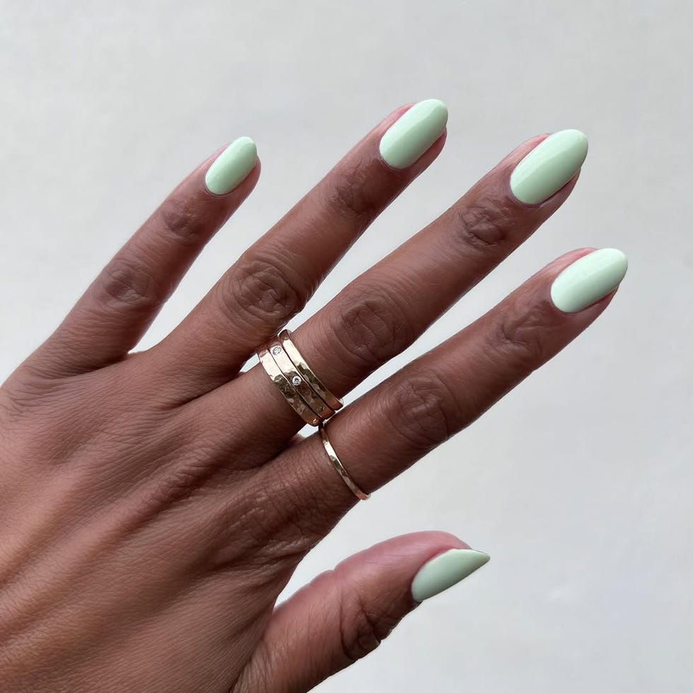 Hand with mint green nails adorned with rings.