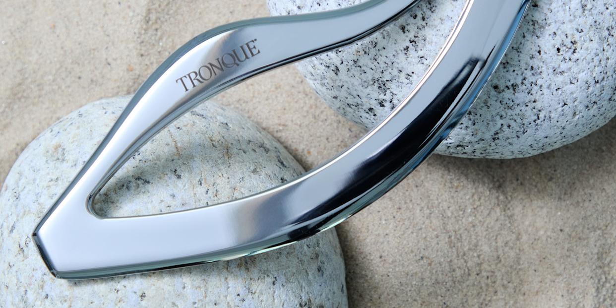 A sleek, metallic tool is placed on smooth, round stones on a sandy surface.