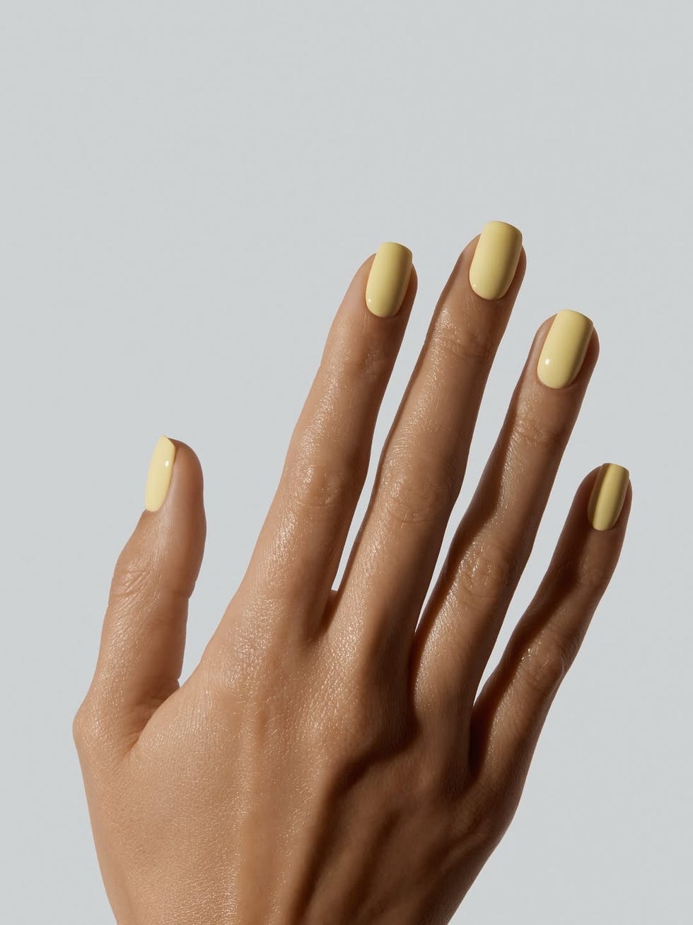 hand with yellow nail polish against a neutral background