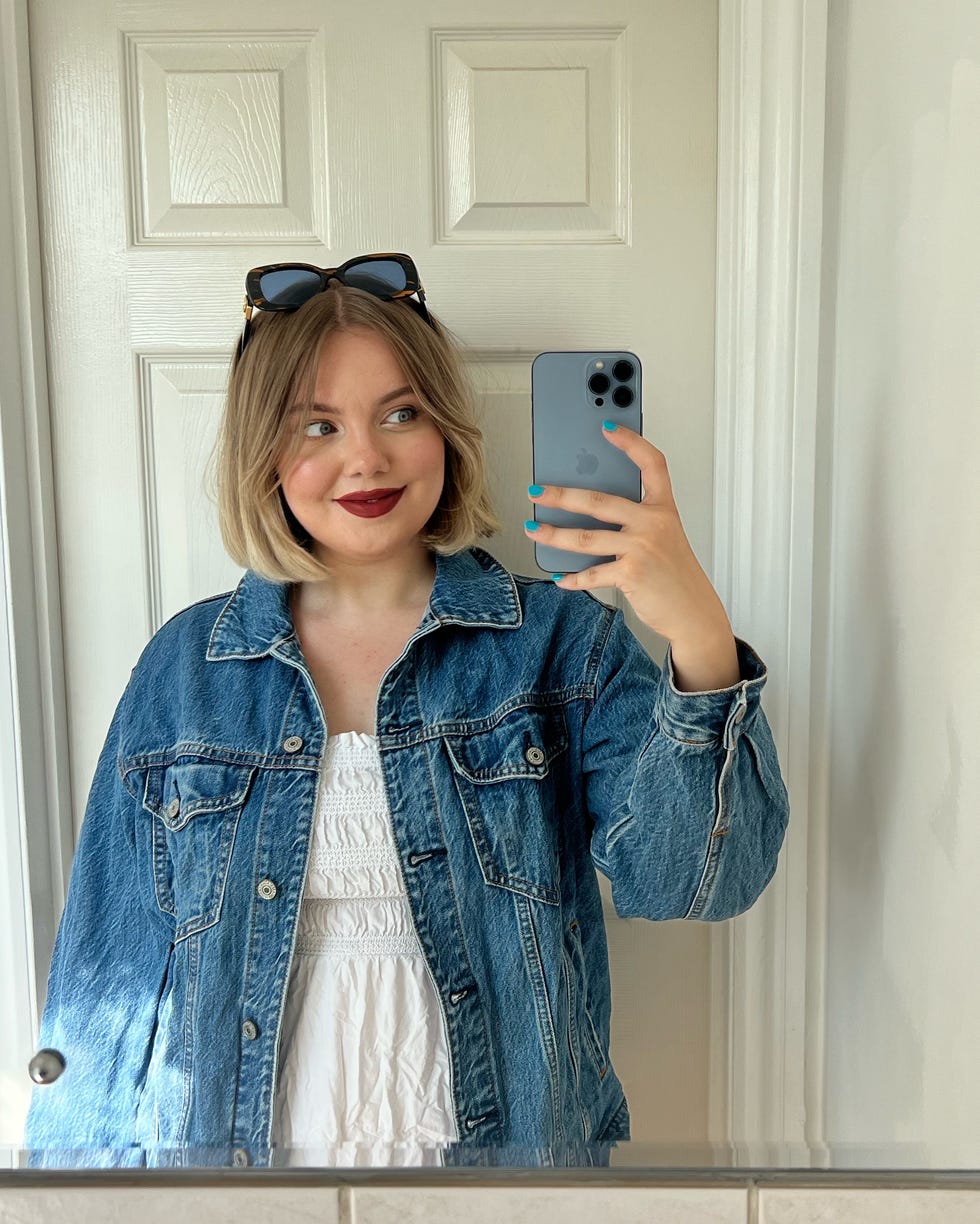 selfportrait in a mirror featuring a woman wearing a denim jacket and holding a mobile phone
