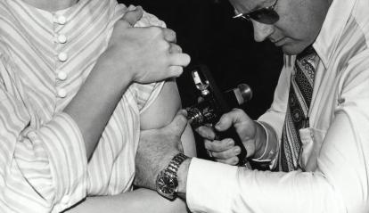 The instrument used by the doctor in the photograph was known as the “peace gun” because of its important role in global smallpox eradication campaigns. These devices used highly compressed air to deliver a jet of vaccine so fine that it penetrated the skin without the need for a needle.