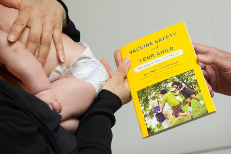 A pediatrician handed a booklet about vaccinations to his client after examining her baby.