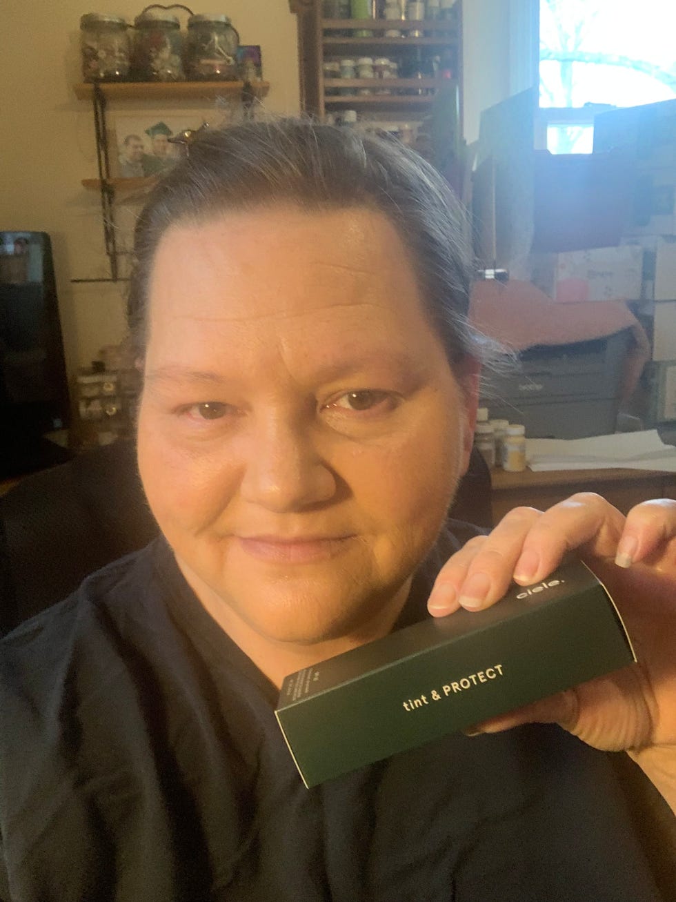User holding a cosmetic product in a room with various containers. User holding a cosmetic product in a room with various containers.