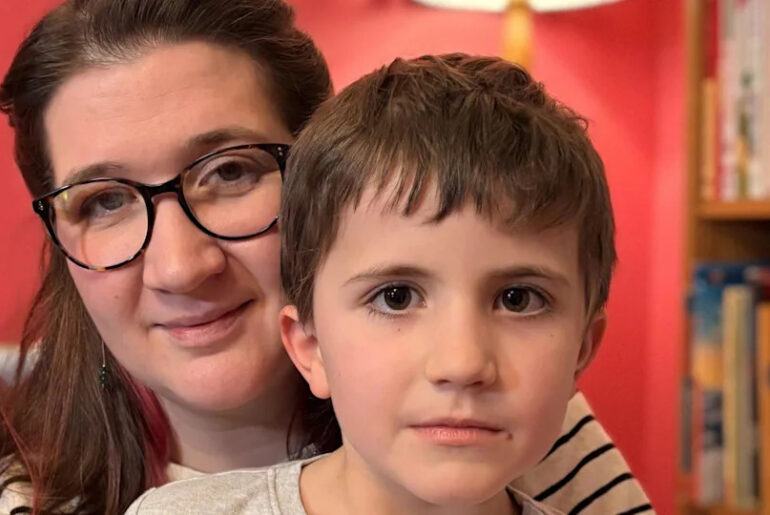 An adult and a young child sitting close together indoors, with bookshelves behind them.