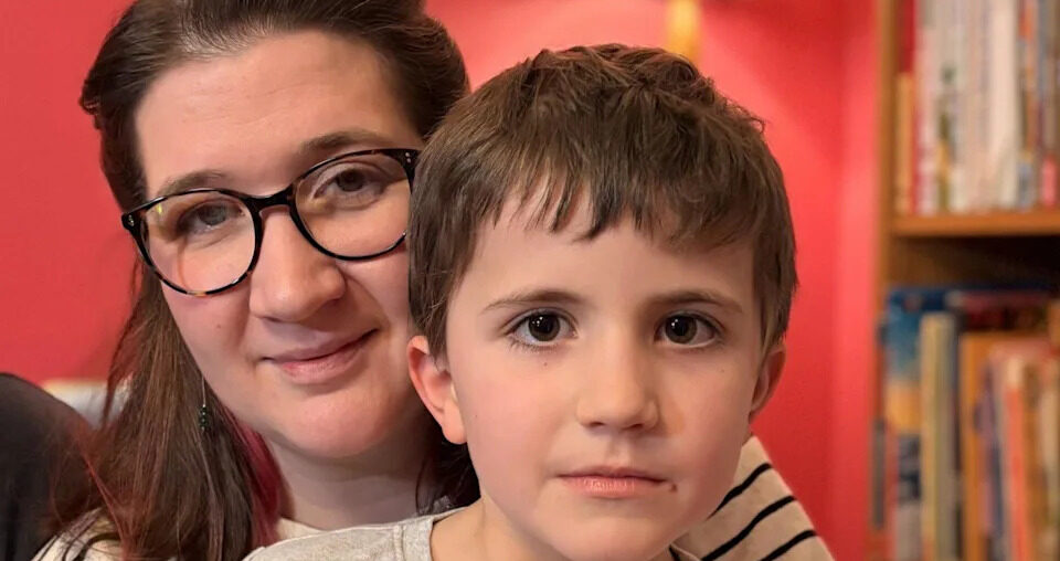 An adult and a young child sitting close together indoors, with bookshelves behind them.