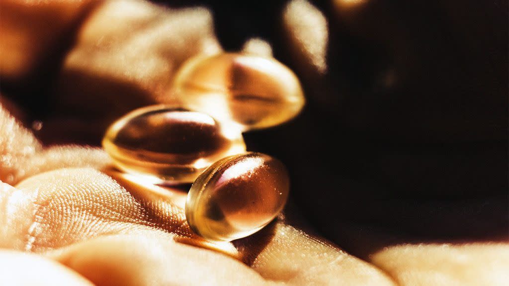 A close-up of vitamin D capsules in a person's hand as sunlight hits them