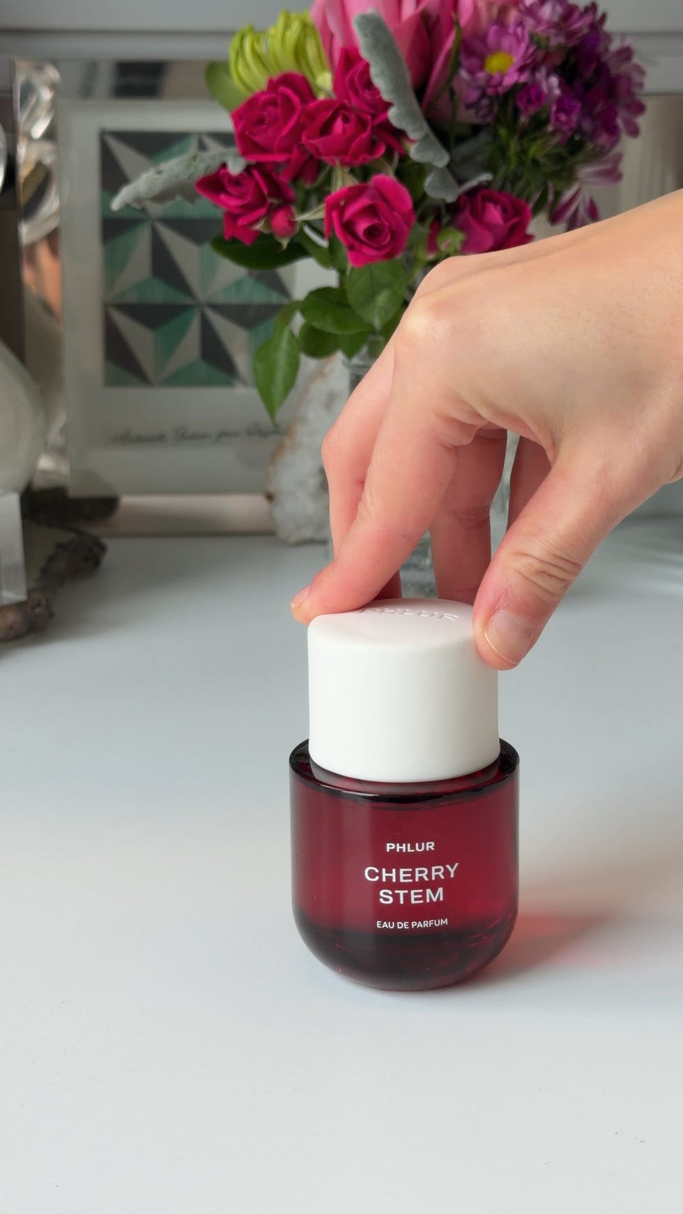 Hand reaching for a perfume bottle on a tabletop.