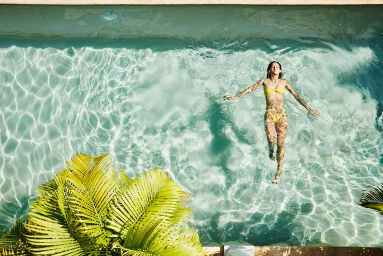 Woman floating in a clear pool at a luxury wellness resort in Mexico.