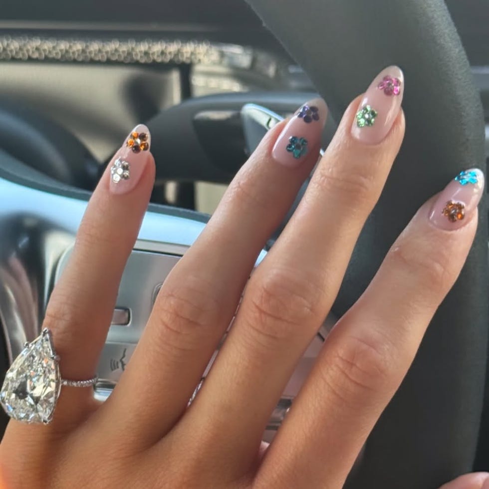 Hand with decorated nails and a ring, positioned on a car steering wheel.