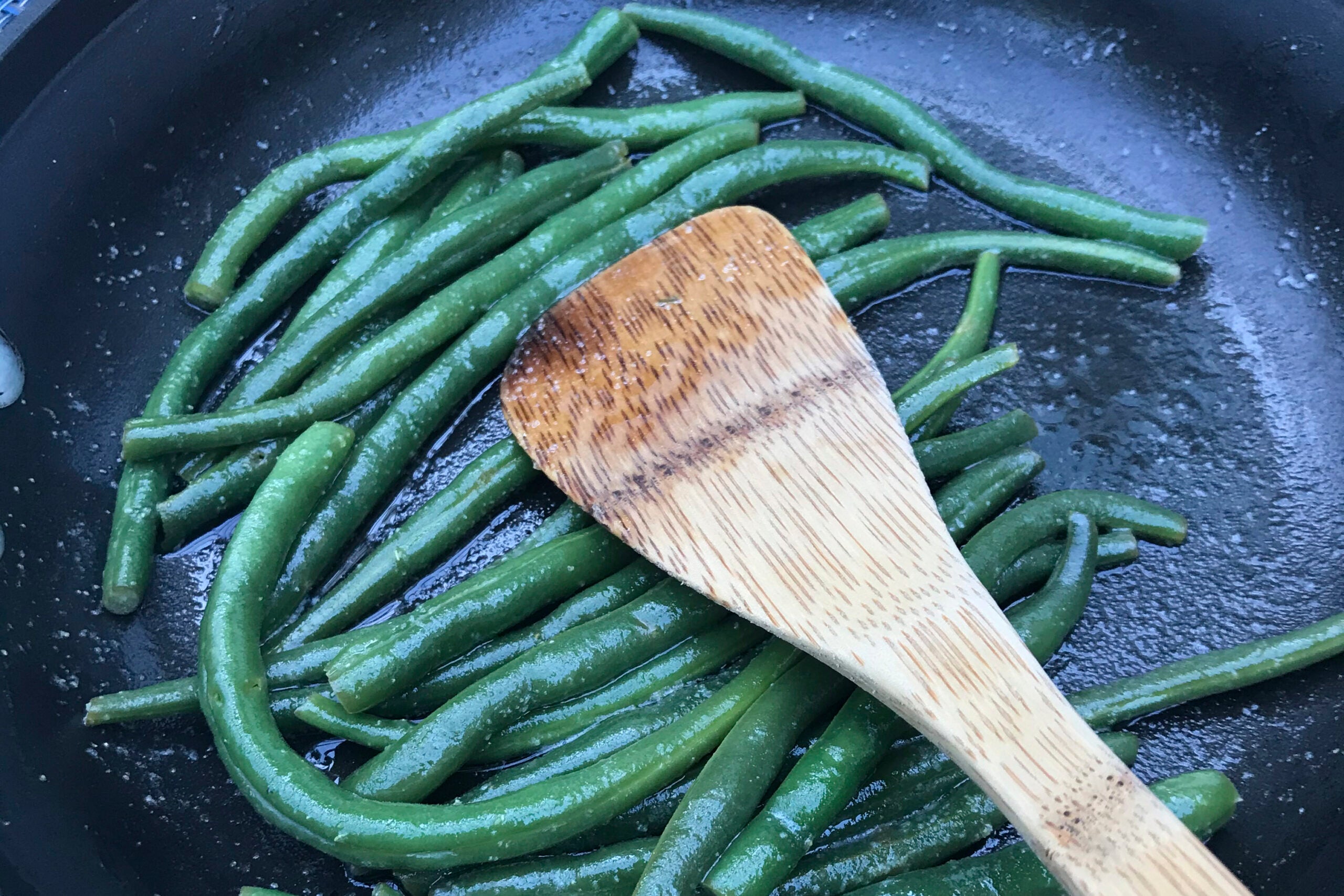 Green beans being sautéed in a pan with a wooden spatula.