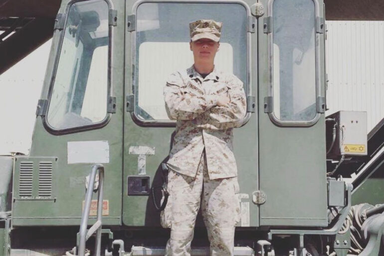 Ali Thompson standing in front of a army truck in Iraq