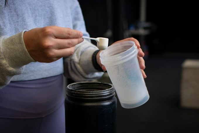 close-up of the hands of an athlete pouring a protein scoop into her shaker