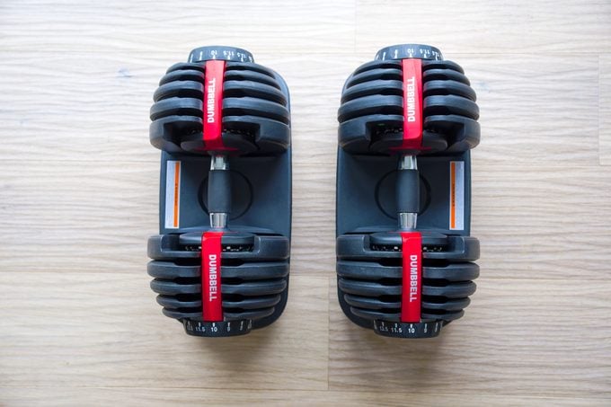High Angle View Of Pair Of Adjustable Dumbbells Against Oak Parquet Floor.
