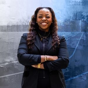A woman smiles with her arms crossed in front of a textured blue background of a track