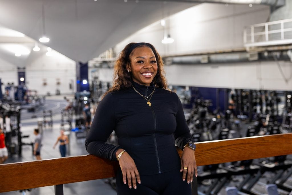 A woman in a black zip-up smiles in a gym
