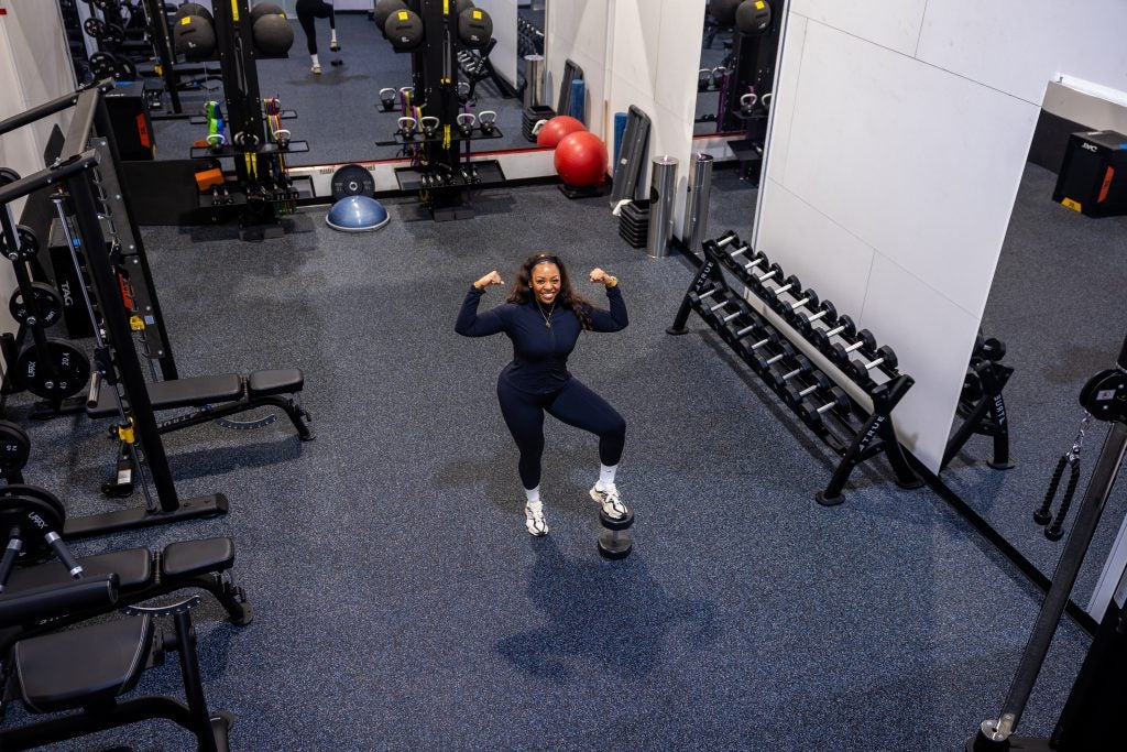 A woman flexes her arm muscles in a gym