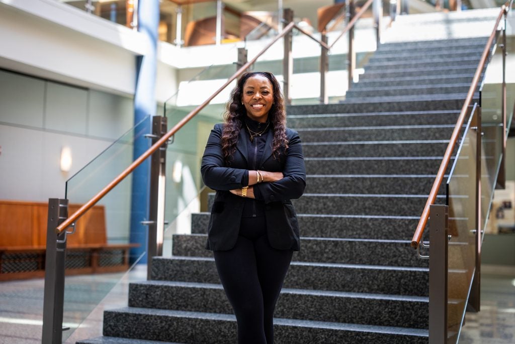 A woman stands in front of a staircase and smiles