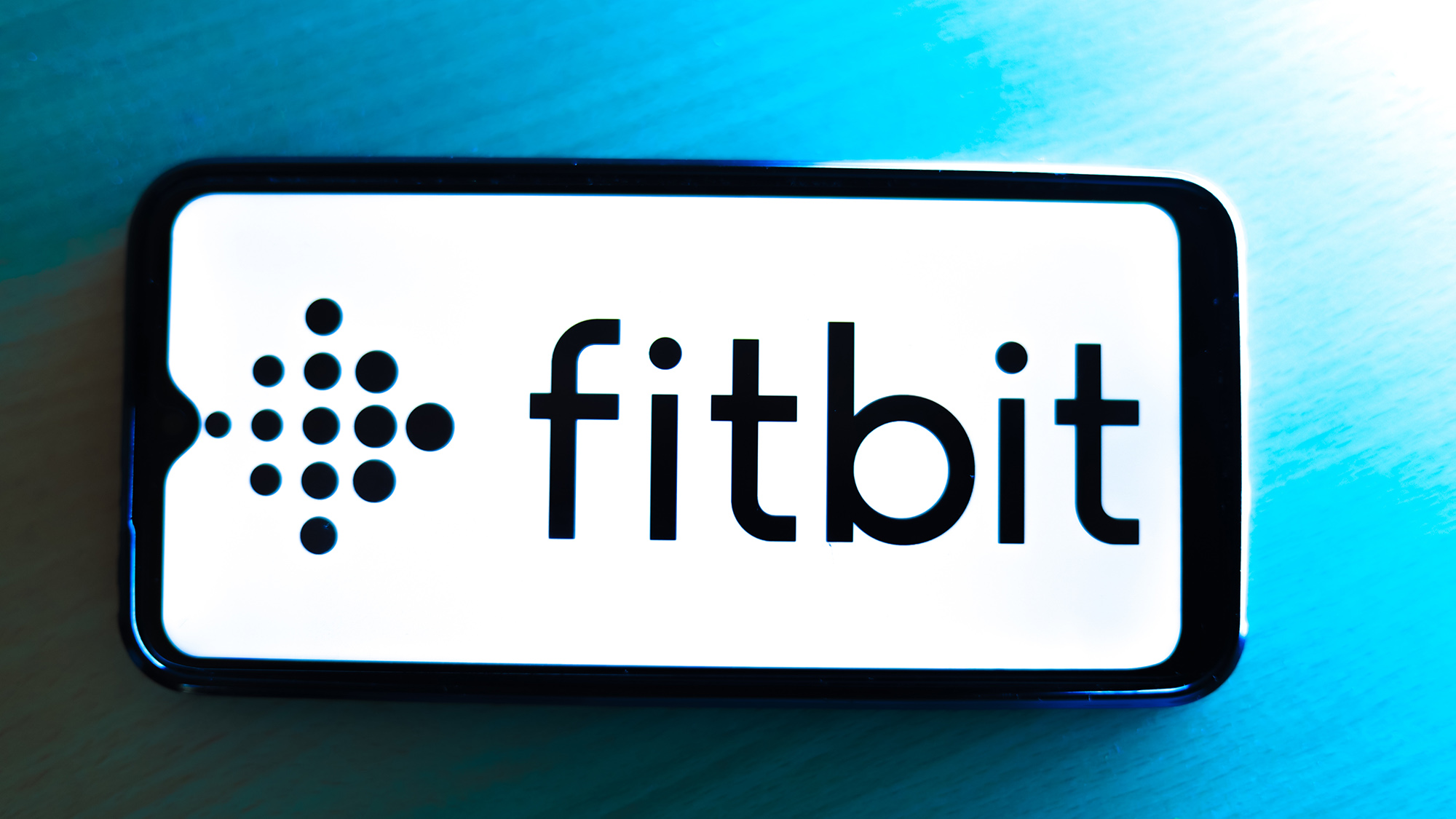 smartphone on laptop keyboard showing Fitbit logo.
