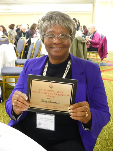Mary wearing a purple suit and holding a certificate at an awards ceremony