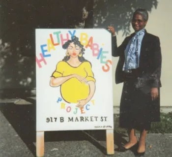 Mary standing by a "Healthy Babies" sign