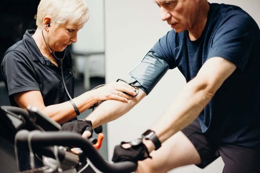 A healthcare professional checks the blood pressure of a man building strength on a stationary bike during personal training at Mountain Brook.
