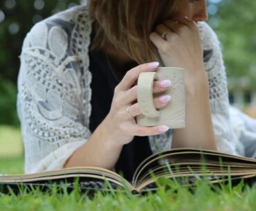 a woman with a mug using simply thick while reading a book in the grass