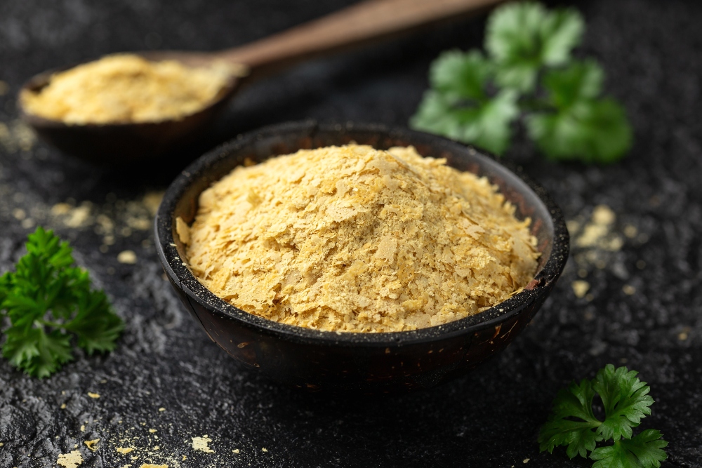 Dried nutritional yeast flakes in a bowl with a spoon in the background, discussed in relation to vitamin B1 and IBS and its potential role in supporting gut health