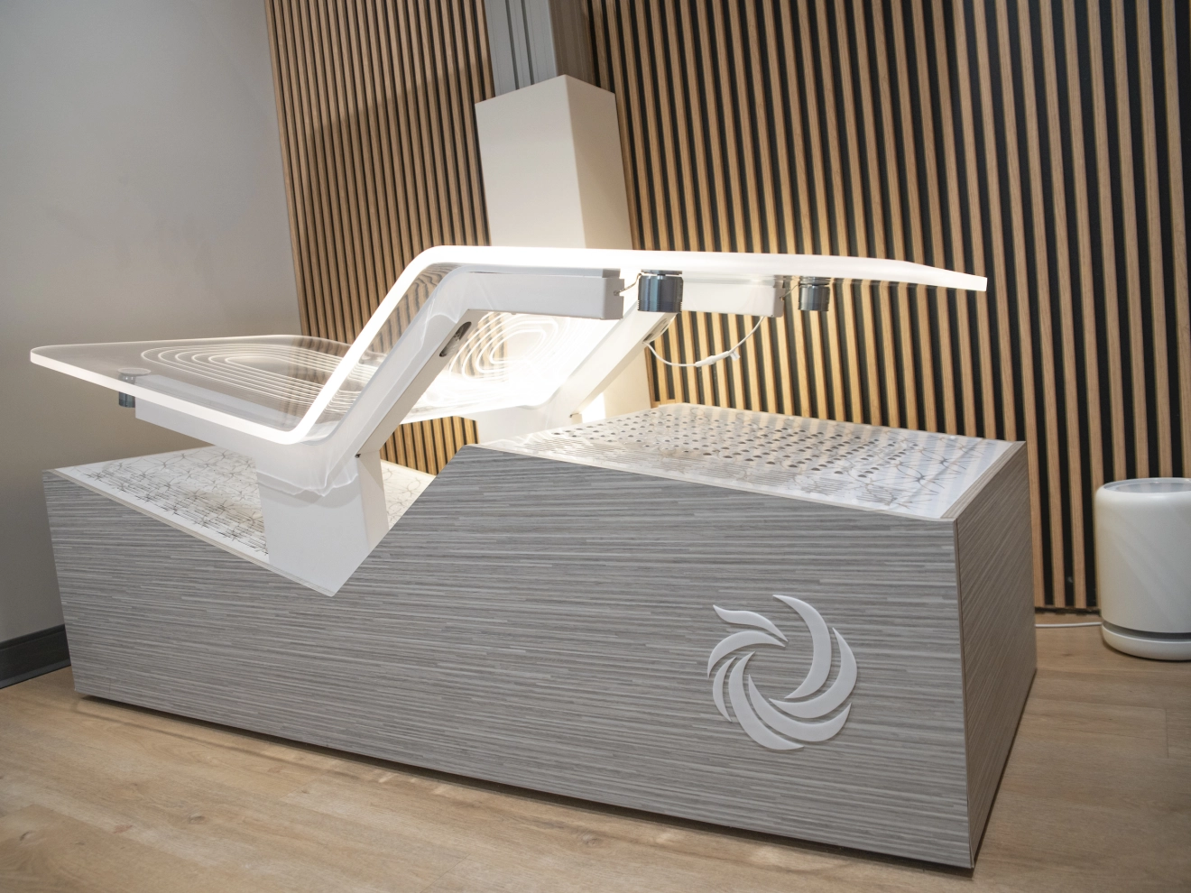 Modern, illuminated dental chair in a clinical room with wooden panel wall and a cylindrical air purifier.