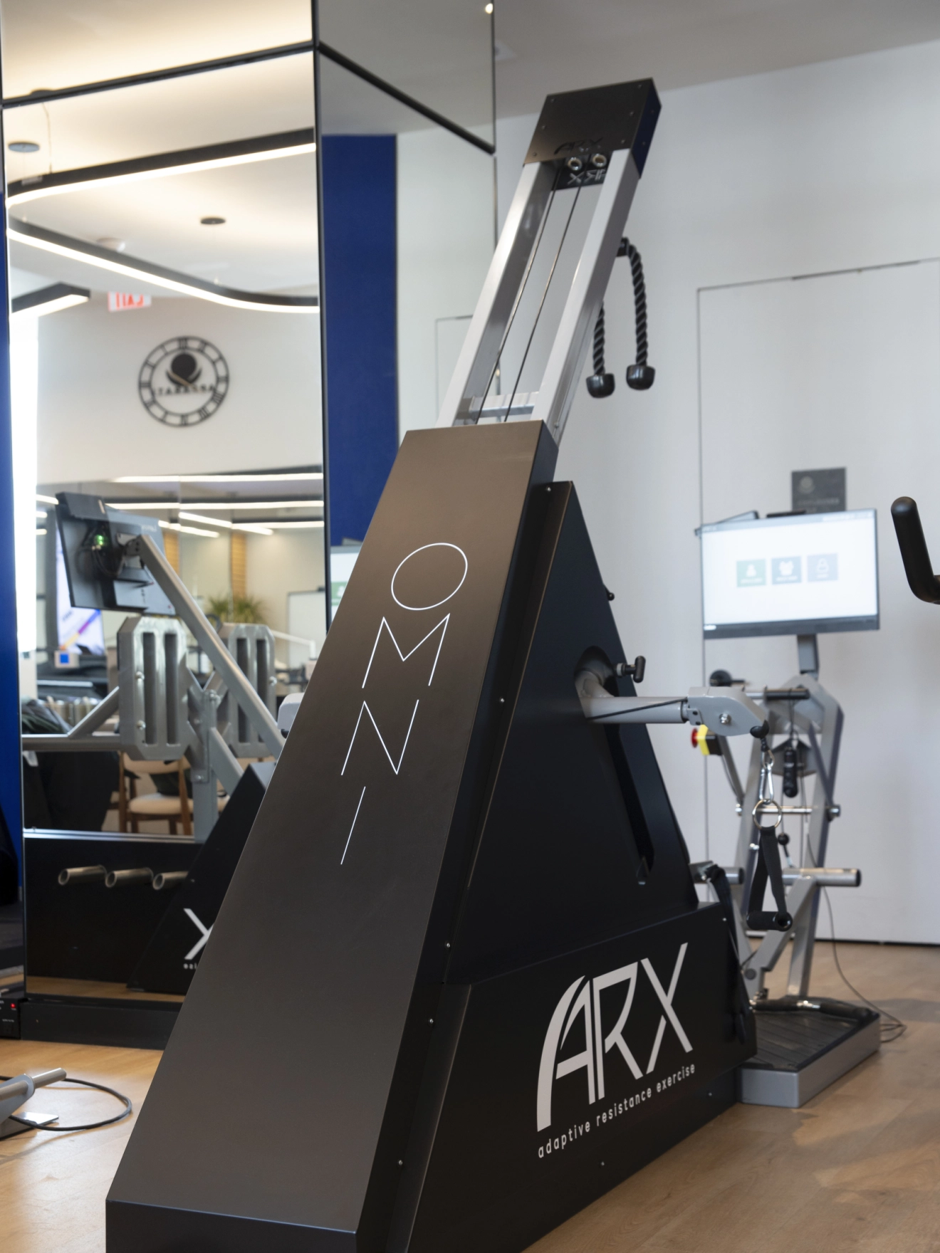 Modern indoor exercise machine in a bright, minimalistic gym with mirrored walls and digital monitors.